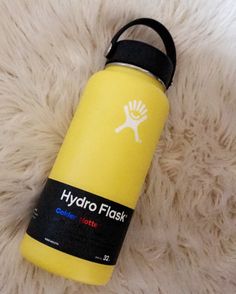 a yellow hydro flask bottle sitting on top of a white fur covered floor with the words hydro flask printed on it