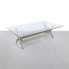 a glass table sitting on top of a gray floor next to a white wall with a wooden frame