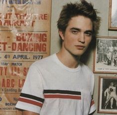 a young man standing next to a wall with posters on it