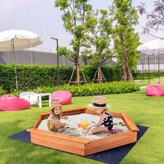 two children playing in a sandbox on the grass with umbrellas and lawn chairs behind them