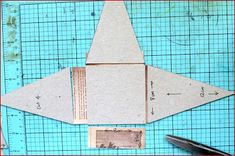 an origami airplane made out of paper on top of a cutting mat with scissors