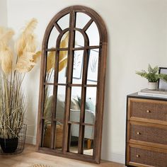 an arched wooden mirror on the wall next to a dresser and potted plant in a living room