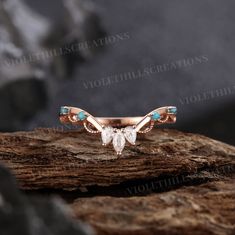 a rose gold ring with turquoise stones and leaves on the side, sitting on top of a rock