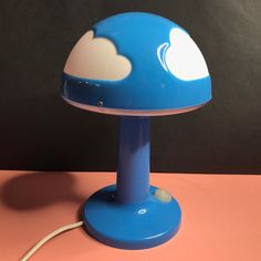 a blue and white mushroom shaped lamp on a pink table with a black wall in the background