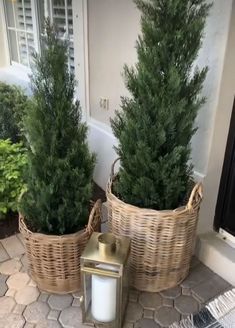 two wicker baskets with trees in them sitting on the front porch next to a lantern