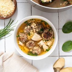 two bowls of soup with meatballs and cheese on the side next to spoons