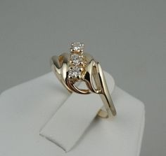 a yellow gold ring with three diamonds on it sitting on a white napkin holder in front of a gray background