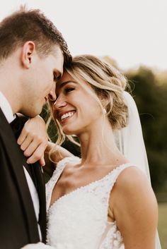 a bride and groom smile at each other as they pose for a wedding photo together