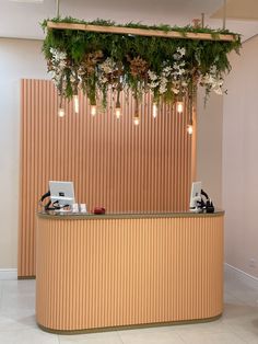 a reception counter with flowers hanging from it's ceiling and laptop on the counter