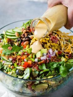 someone pouring dressing onto a salad in a glass bowl