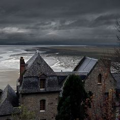 an old building on the edge of a body of water under a dark cloudy sky