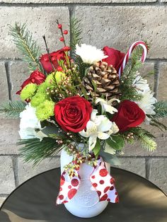 a vase filled with red roses and white flowers on top of a table next to a brick wall