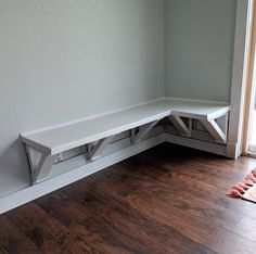 a corner bench in the corner of a room with wood flooring and white walls