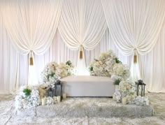 a white wedding ceremony setup with flowers and candles in front of drapes on the wall