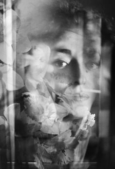 a black and white photo of a man with flowers in front of him, looking out the window