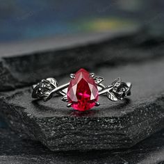 a close up of a ring with a red stone in the middle and leaves around it