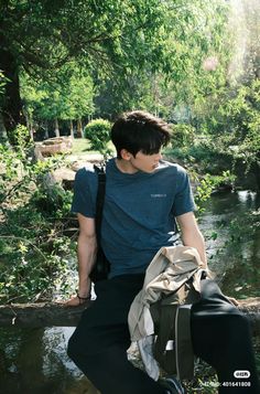 a young man is sitting on a log in the woods with his back to the camera