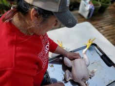 a woman in a red shirt is cutting up a chicken on a tray with scissors