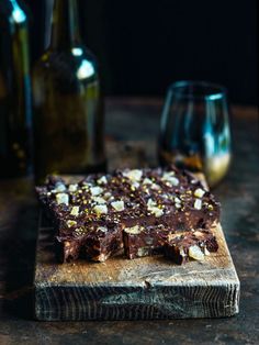 a wooden cutting board topped with brownies and nuts next to two bottles of wine