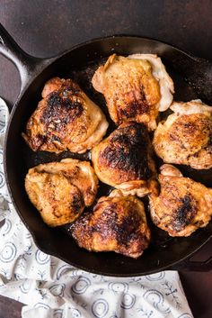 chicken thighs in a cast iron skillet on a wooden table with a cloth next to it