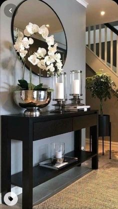 a black table with flowers and candles on it in front of a stair case, next to a round mirror