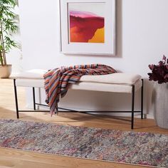 a white bench sitting on top of a hard wood floor next to a rug and potted plant