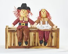 two scarecrow dolls sitting on top of a wooden bench