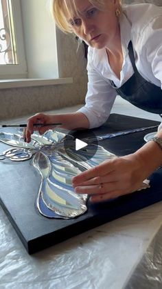 a woman in white shirt and black apron working on art work with glass butterfly design