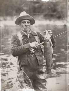 an old photo of a man holding a fish in his hand while standing in the water