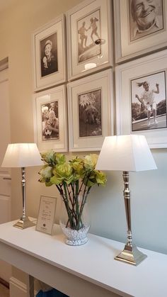 a white table topped with two lamps next to pictures on the wall and flowers in a vase