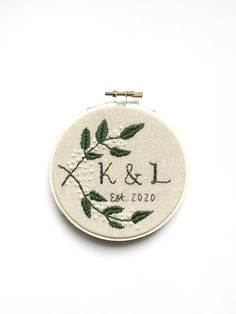 a white embroidery hoop with green leaves on it and the words k & l embroidered in black ink