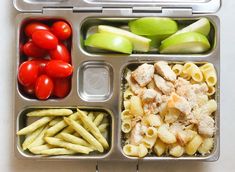 a lunch box filled with pasta, tomatoes and green apple slices on top of it