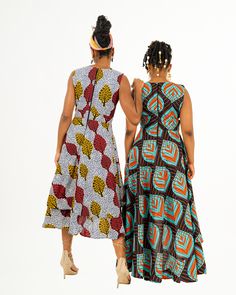 Two women posing in a red blue and black African print maxi dress and a yellow red and white African print maxi dress. Multicolor Print Sleeveless Midi Sundress, Sleeveless Multicolor Sundress Midi Dress, Fitted Sleeveless Maxi Dress With Layered Hem, Multicolor Printed Dress With Asymmetrical Hem, Multicolor Asymmetrical Dress With Print, Bohemian Sleeveless Multicolor Midi Dress, Multicolor Handkerchief Hem Dress, Bohemian Sleeveless Midi Dress In Multicolor Print, Multicolor Printed Maxi Sleeveless Dress