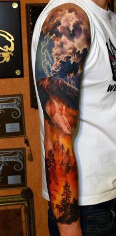 a man's arm with a mountain scene on it and clouds in the sky