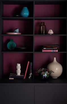 a shelf with vases, books and other items on it in front of a purple wall