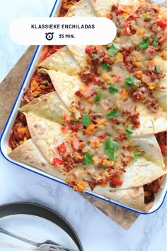 a casserole dish with tortilla shells and salsa on the side next to a pair of utensils