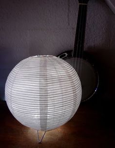 a white paper lantern sitting on top of a wooden table next to a ukulele