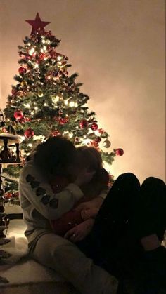 two people sitting next to each other in front of a christmas tree with the lights on