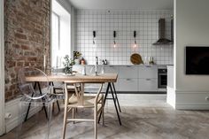 an open kitchen and dining area with brick walls, white cabinets and wooden table in the center