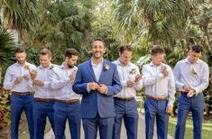 a group of men standing next to each other in front of palm trees and bushes