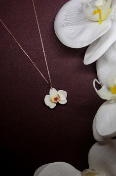 a necklace with a flower on it sitting next to some white orchids and flowers