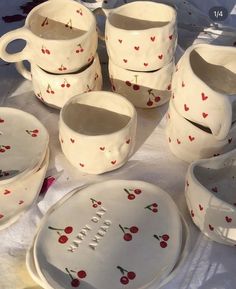 a table topped with lots of white dishes and bowls covered in cherries painted on them