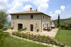 an old stone house in the countryside surrounded by flowers and greenery, on a sunny day