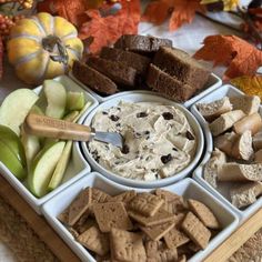 an assortment of snacks arranged in trays on a table with apples, pumpkins and leaves