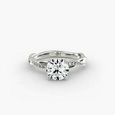 a white gold engagement ring with diamonds on the band and a round cut diamond in the center