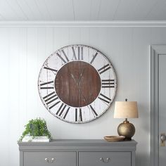 a large clock mounted to the side of a wall next to a dresser and lamp