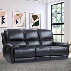 a black leather couch sitting in front of a window next to a wall with pictures on it