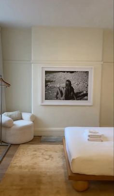 a white bed sitting in a bedroom next to a chair and pictures on the wall