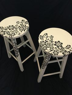 two white stools with black and white designs on the top one has a flower design on it