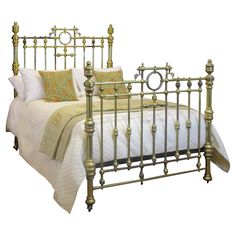 a gold metal bed with white sheets and pillows on it's headboard, in front of a white background